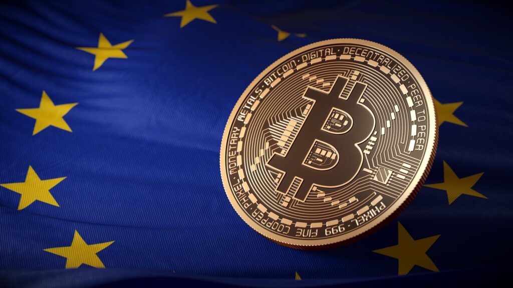 Gold Bitcoin coin resting on a blue European Union flag with yellow stars, close-up image about crypto in Europe.