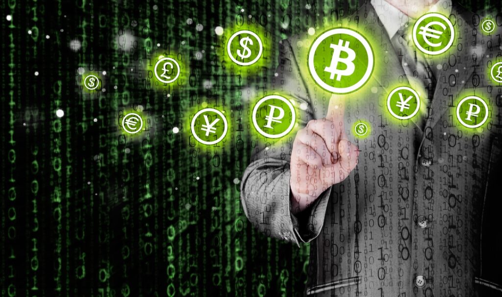 Choosing bitcoins businessman pressing touch screen button - Crypto-Globe.com Professional in a suit reaches toward glowing green cryptocurrency symbols (Bitcoin, Yen, Ruble, Dollar) against a binary digital background.