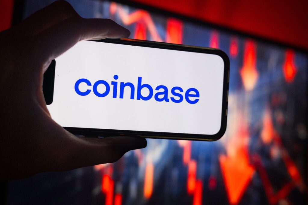 Smartphone held in a hand displaying the Coinbase logo on a white screen.